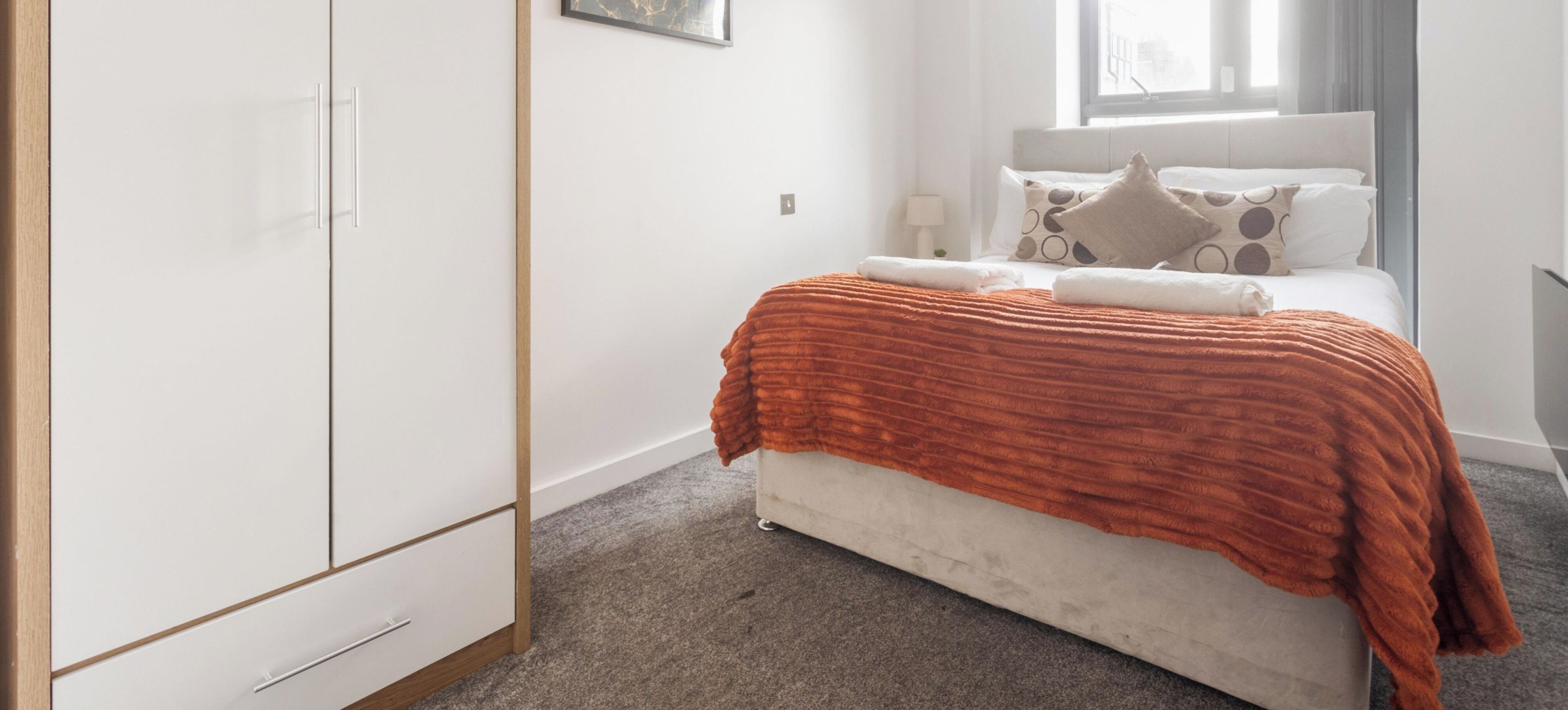 A bedroom with a bed, a wardrobe, a window, and a lamp.