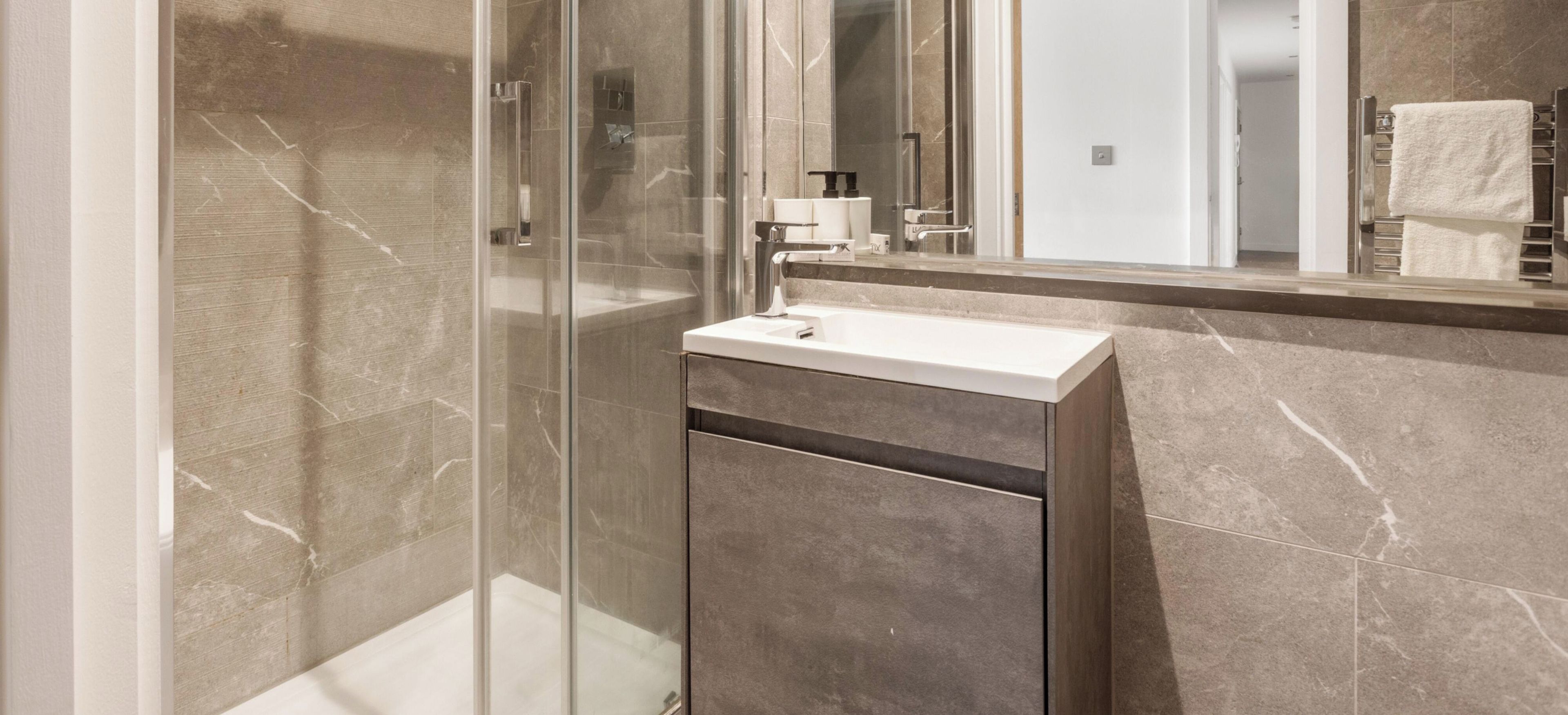 A modern bathroom with a glass shower enclosure, a white sink, and a marble-tiled wall.