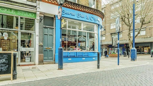 Et gadesyn med en butik i blå farver, der hedder 'Sunrise Fish & Chips', og en 'Pickle Studio' på den anden side af vejen.