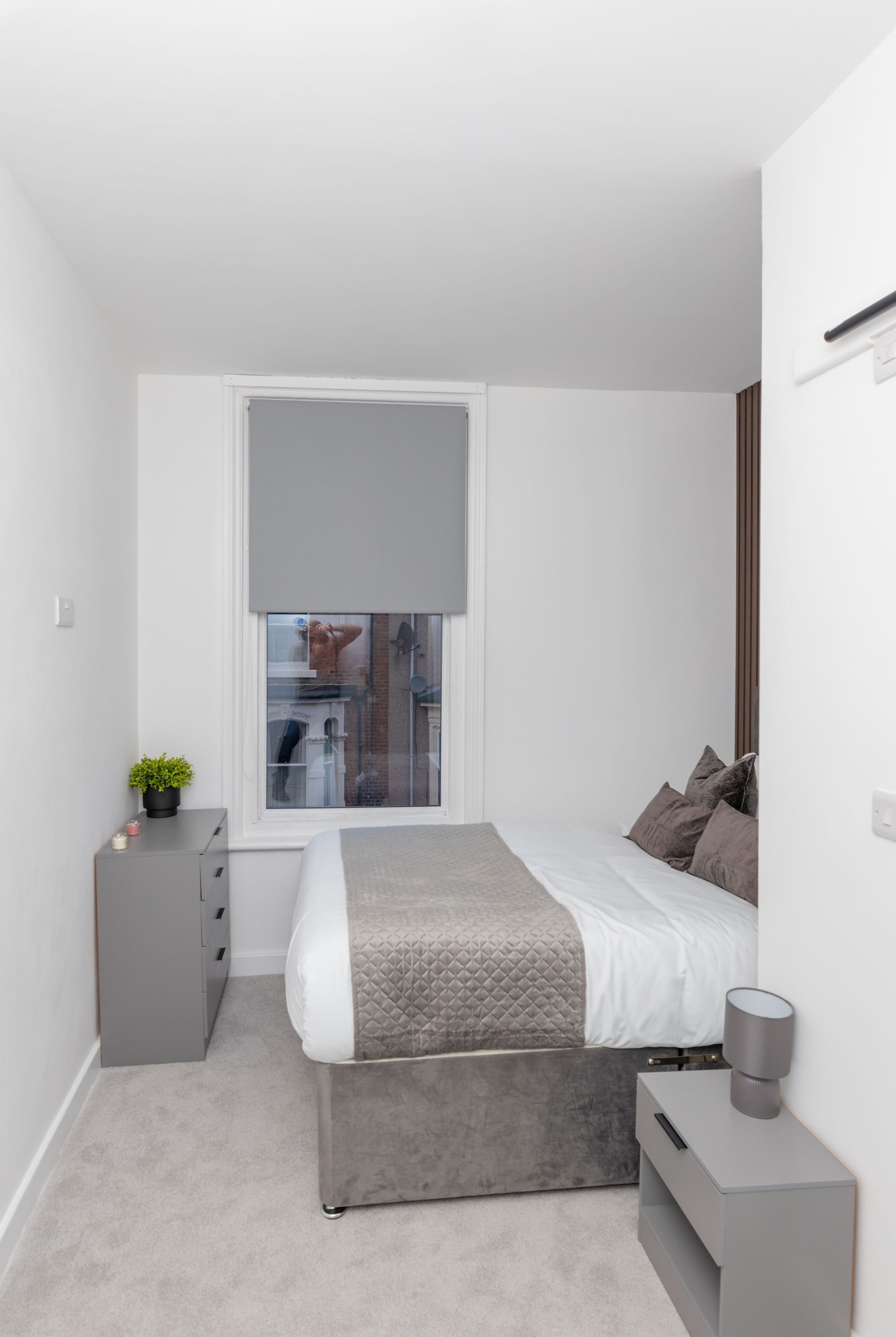 Een moderne slaapkamer met een bed, nachtkastje en een raam met jaloezieën.