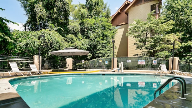 A swimming pool with lounge chairs and a covered seating area, surrounded by a fence and trees. - Gatlinburg Town Village  (Gatlinburg)