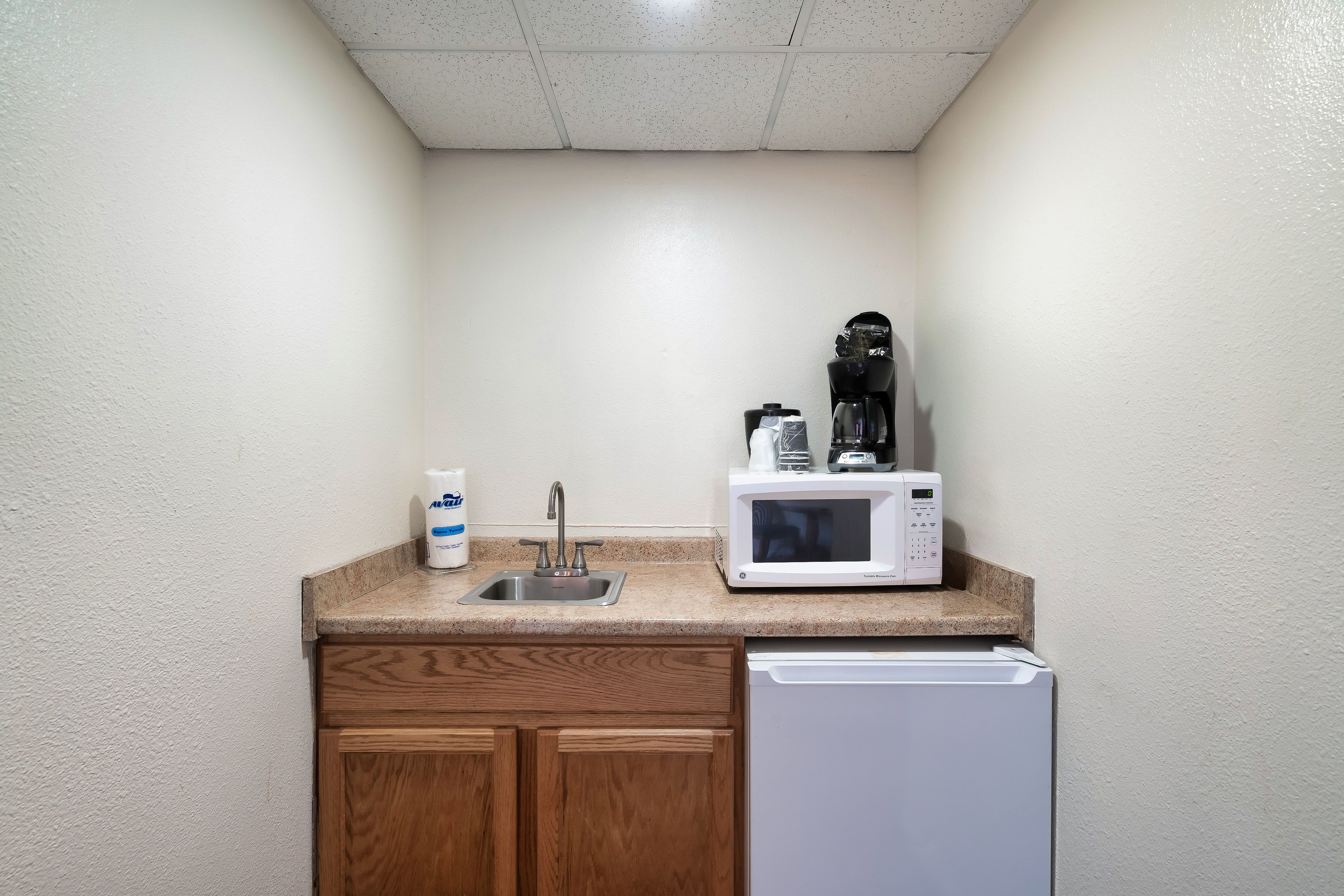 Una kitchenette con un lavamanos de acero inoxidable, un microondas y una cafetera sobre una encimera de granito.