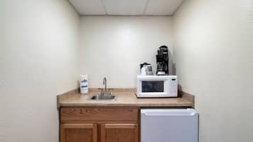 Una kitchenette con un lavamanos de acero inoxidable, un microondas y una cafetera sobre una encimera de granito.
