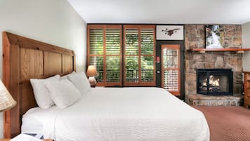 Ein Schlafzimmer mit einem großen Bett, einem Kamin aus Stein und Blick auf grüne Natur durch das Fenster.