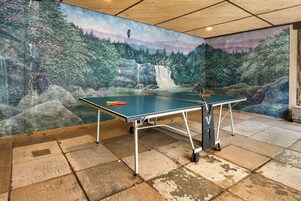Una mesa de ping pong en una habitación con un mural que muestra un bosque y una cascada.