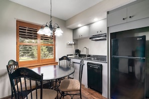 A modern kitchen with a dining table, chairs, a refrigerator, and a window with blinds. - Gatlinburg Town Village  (Gatlinburg)
