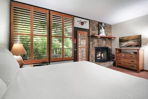 A bedroom with a bed, a fireplace, a stone wall, and a television. - Gatlinburg Town Village  (Gatlinburg)
