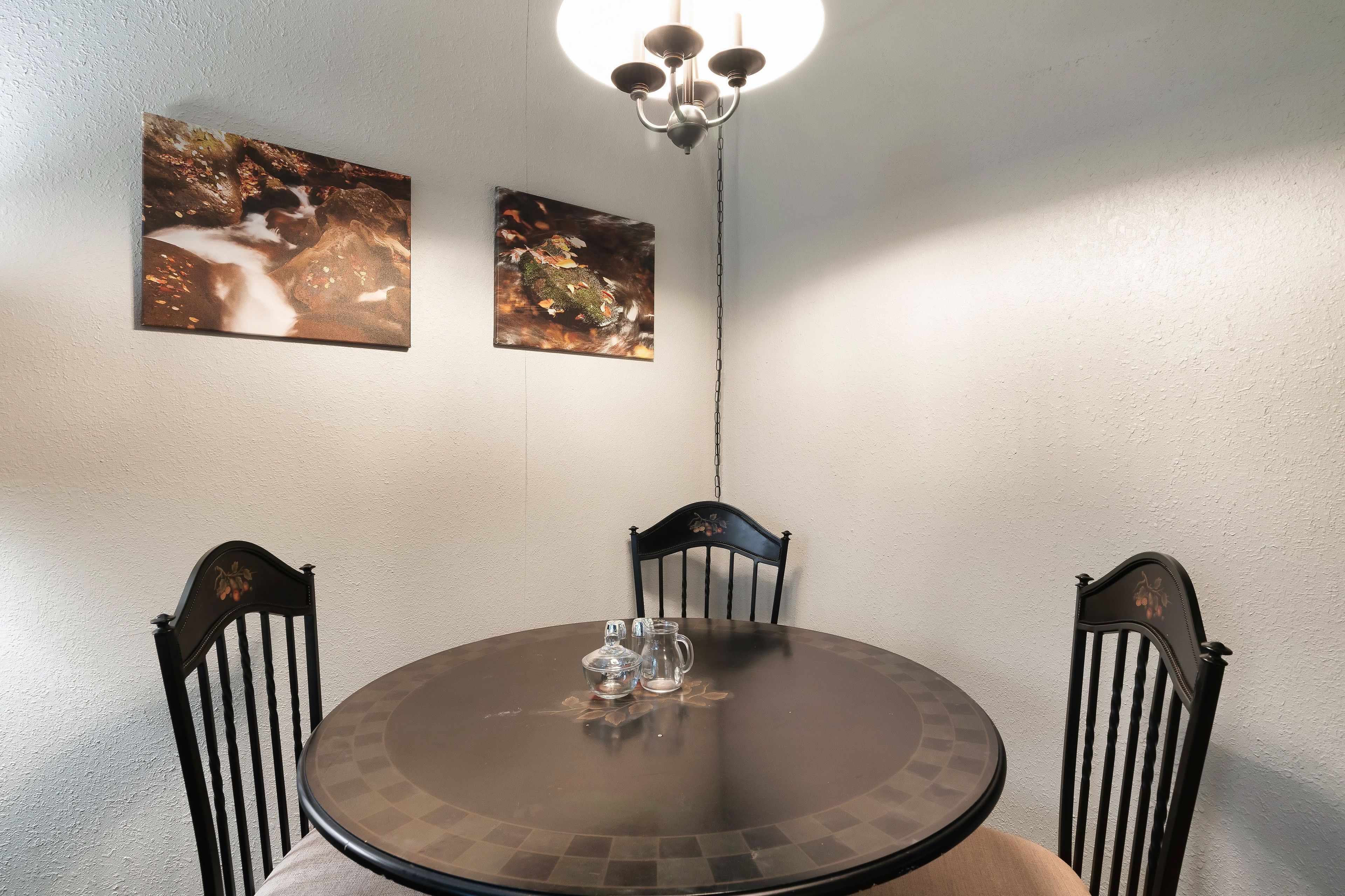 Ein Essbereich mit einem runden Tisch, vier Stühlen, zwei Bildern an der Wand und einer Pendelleuchte.