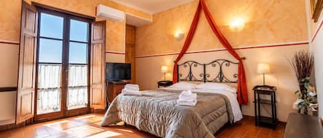 Un dormitorio con cama, televisión, ventana con cortinas, aire acondicionado montado en la pared y lámpara de noche.