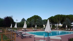 Zona de piscina con sillones de descanso, sombrillas y una pileta.