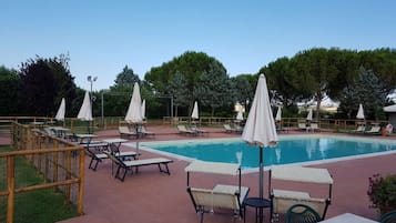 Zona de piscina con sillones de descanso, sombrillas y una pileta.