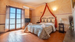 Una habitación de hotel con cama, televisor, ventana con cortinas, aire acondicionado instalado en la pared y piso de baldosas.