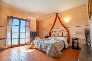 Quarto de hotel com cama, televisão, janela com cortinas, ar condicionado fixado na parede e chão em azulejos.