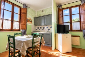 Una cocina con una mesa de comedor, sillas, un refrigerador y un televisor.