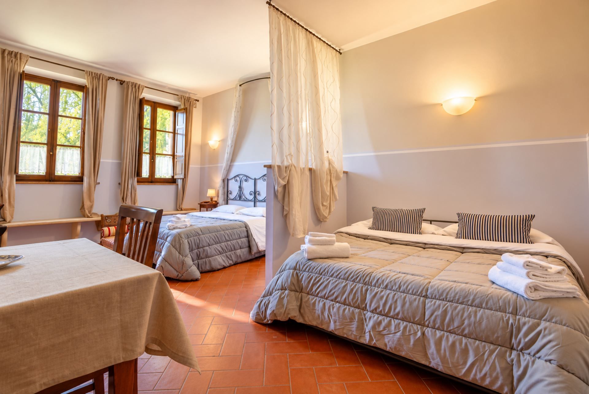 Una habitación de hotel con dos camas, una mesa de comedor y una ventana con cortinas.