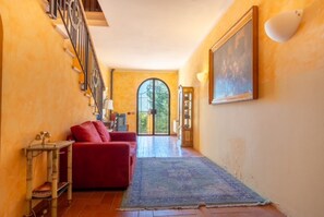 Un pasillo con un sofá rojo, una mesita, un tapete azul, una escalera y un cuadro grande en la pared.