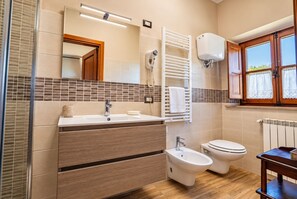 Un baño con tocador de madera, un bidé, un inodoro y una ventana con cortinas.