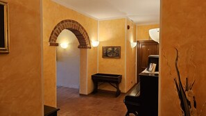 Un passadís amb una arcada de maó, una banca de fusta, un escriptori amb una làmpada i una fotografia emmarcada a la paret.