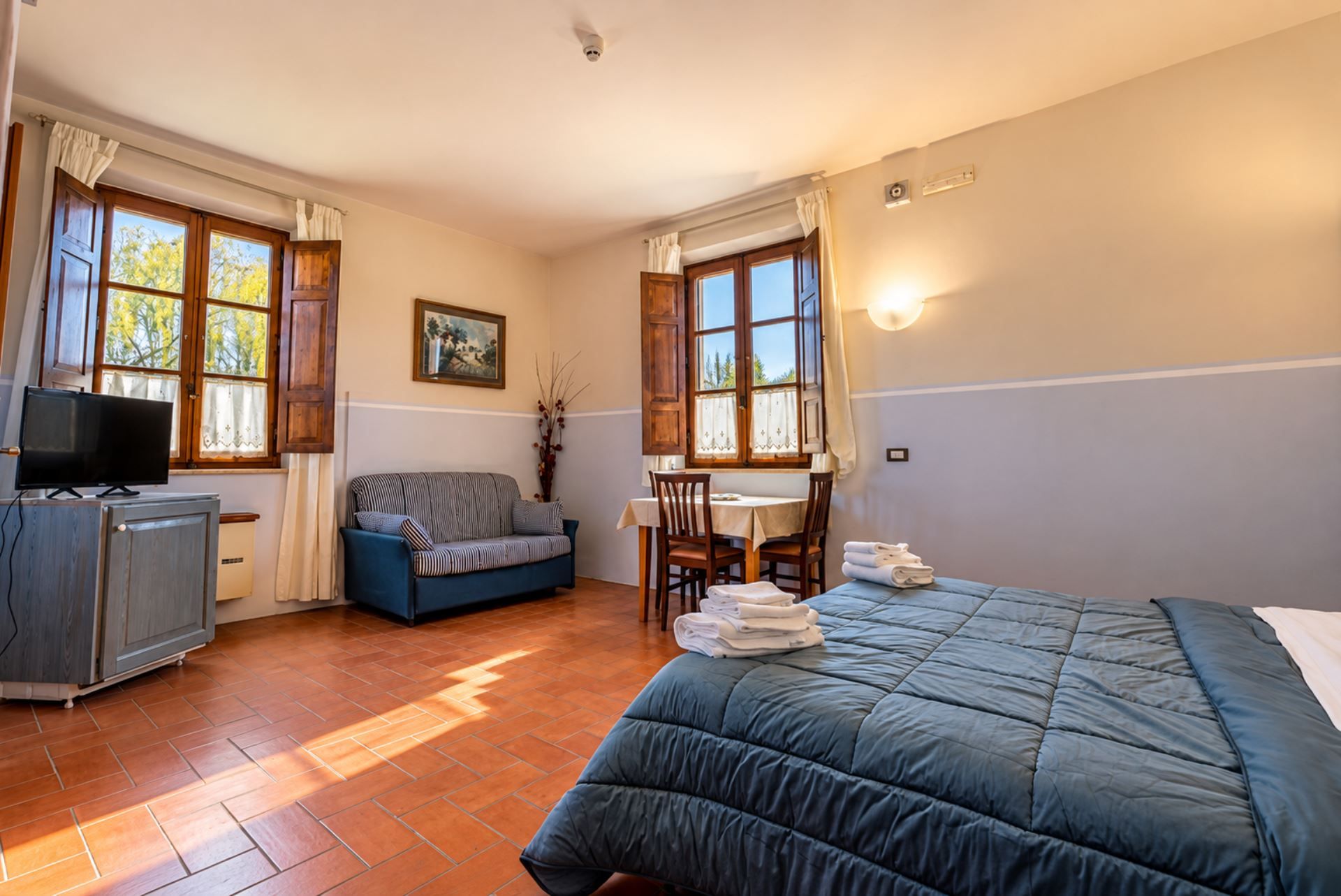 Habitación de hotel con cama, sofá, escritorio con sillas, televisión y ventana con cortinas.