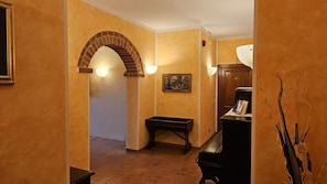 Un corridoio con un arco in mattoni, una panca di legno, una scrivania con una lampada e un quadro appeso al muro.