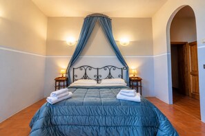 Un dormitorio con cama a dosel, dos lámparas de noche y una puerta que da a otra habitación.