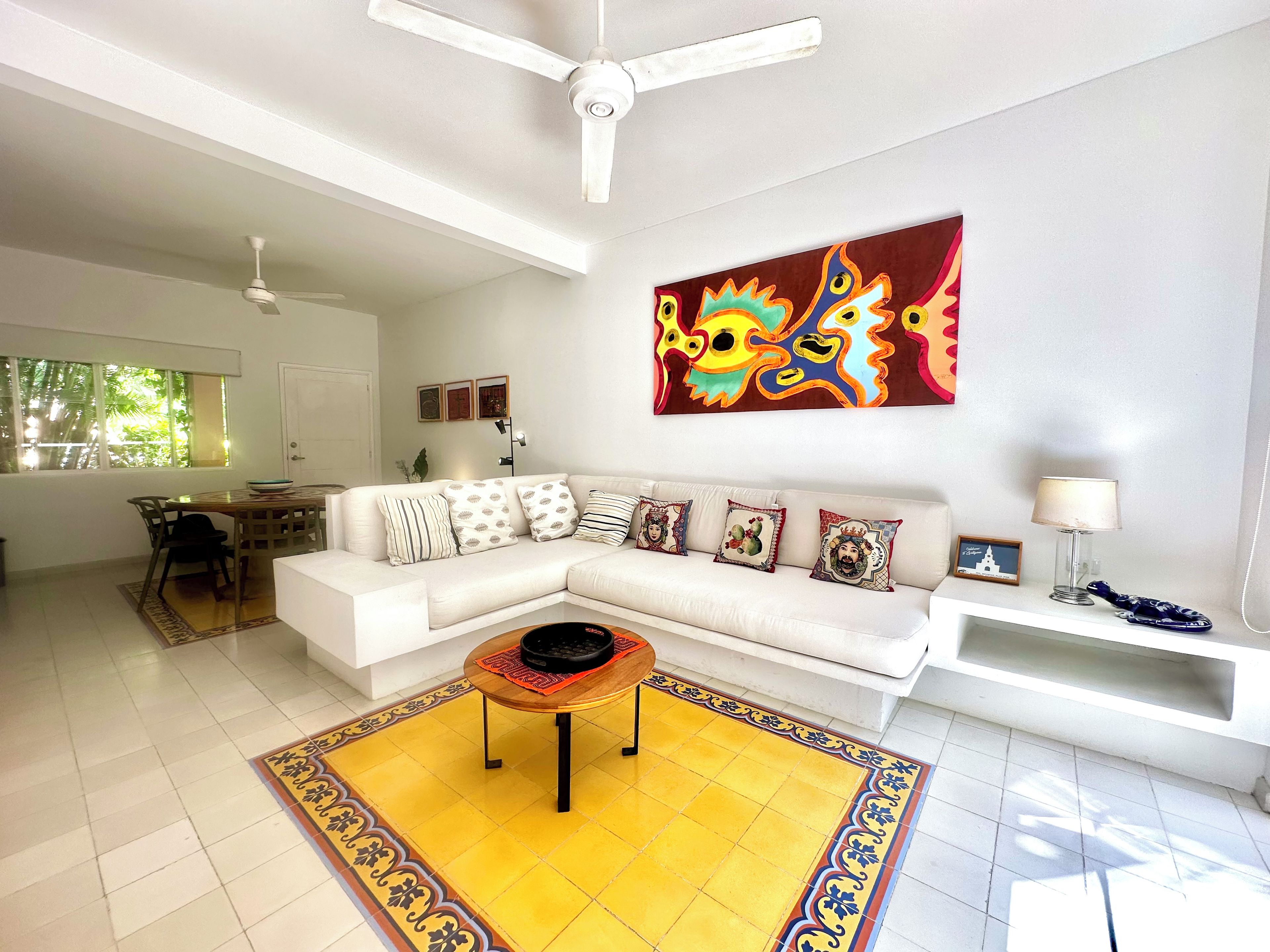 A modern living room with a white sofa, a coffee table, and a colorful abstract painting on the wall.