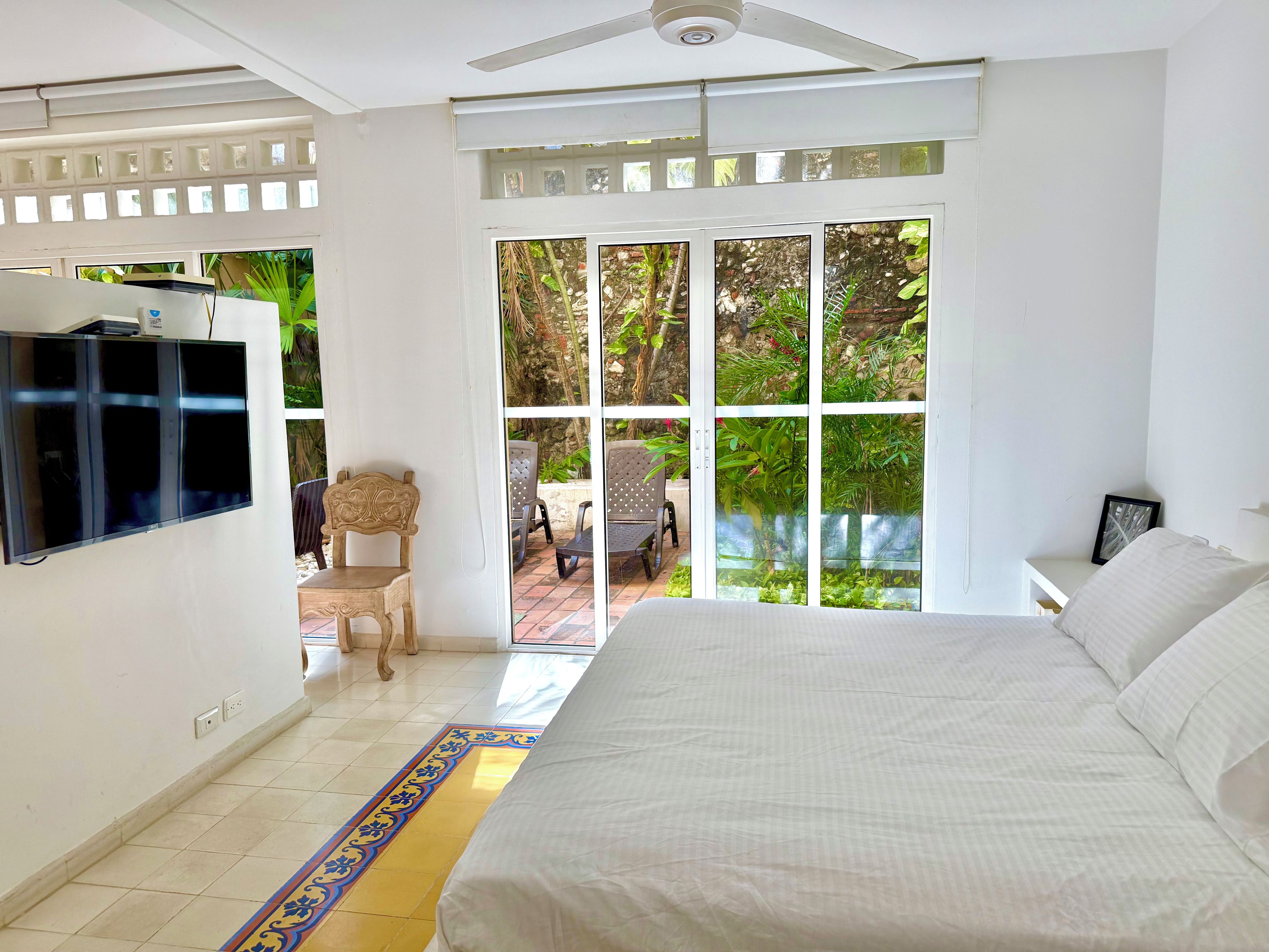 Un dormitorio con cama, televisor y vista a un patio exterior con sillas y plantas.