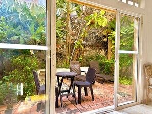 A patio area with a table and chairs, a stone wall, and tropical plants. - by Calamari.Homes - Centenario Casa 102 - Old City (Cartagena de Indias)