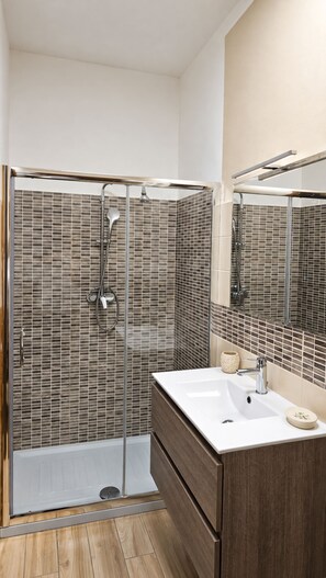 Un baño moderno con cabina de ducha acristalada, lavabo blanco y tocador de madera.