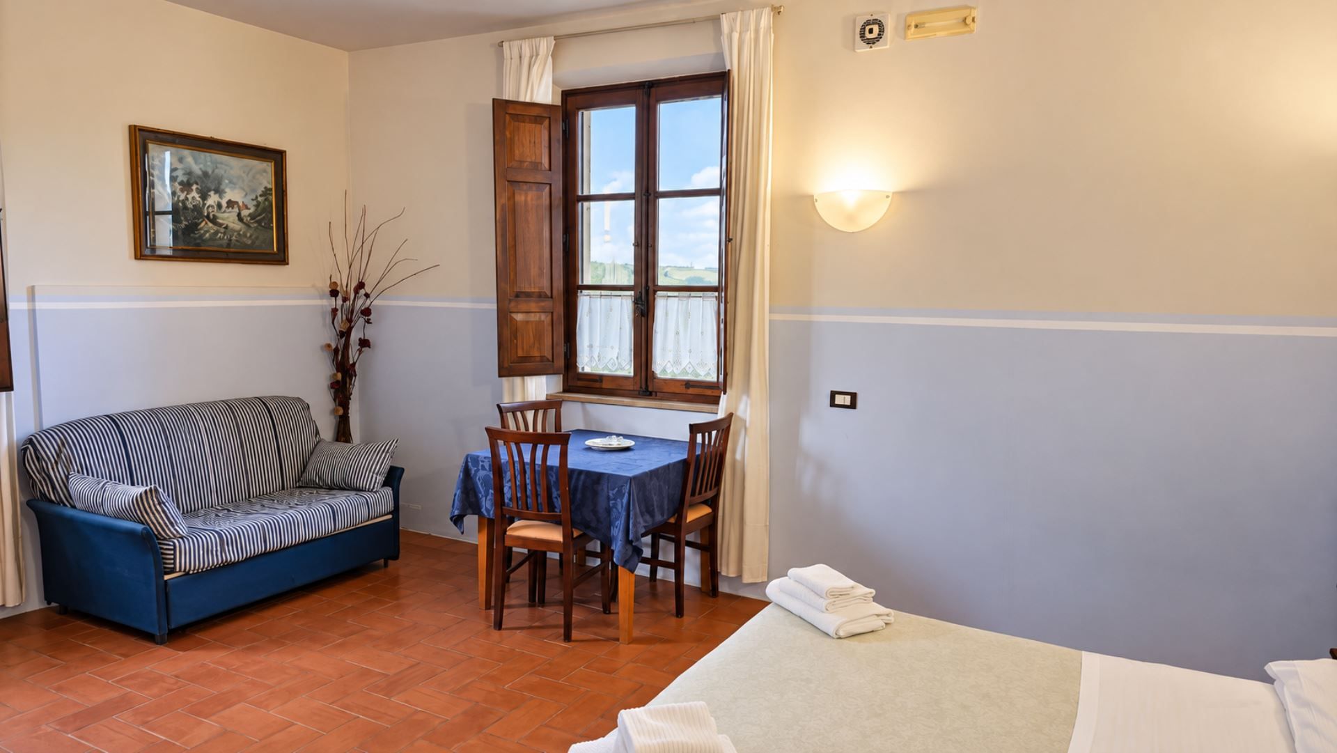 Una habitación con sofá, una mesa de comedor con sillas, una ventana con cortinas y una cama.