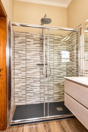Un box de ducha moderno con puerta de cristal, ducha de lluvia y pared con azulejos.