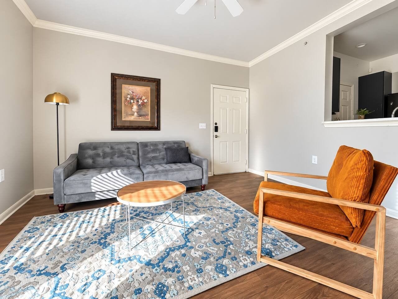 A living room with a grey sofa, a wooden coffee table, a patterned rug, a tall floor lamp, and a wooden chair with a cushion.