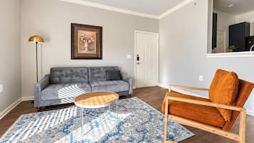 A living room with a grey sofa, a wooden coffee table, a patterned rug, a tall floor lamp, and a wooden chair with a cushion.
