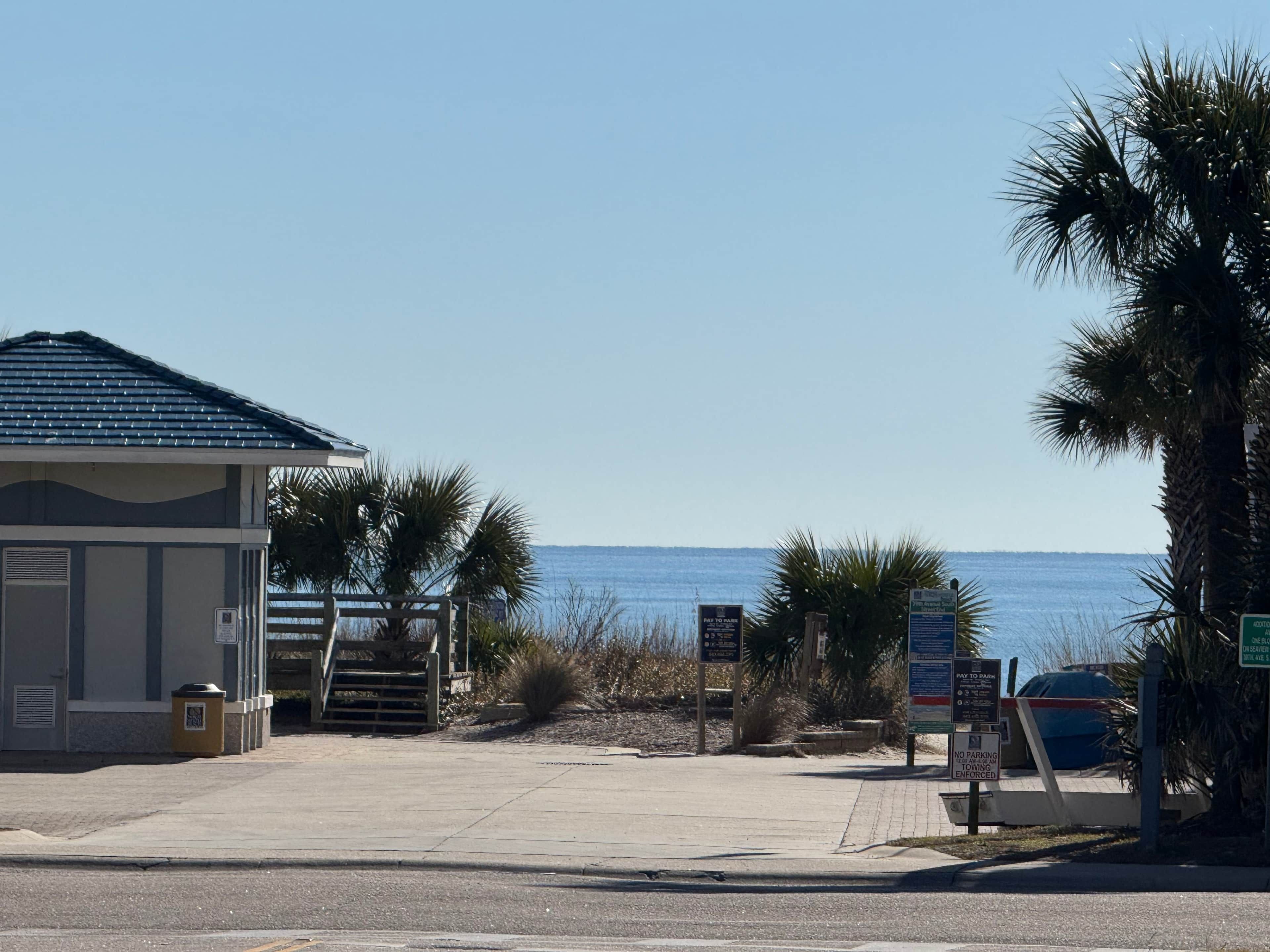 Un bâtiment situé en bord de mer, doté d’une entrée sécurisée par un portail, de palmiers et offrant une vue dégagée sur l’océan.