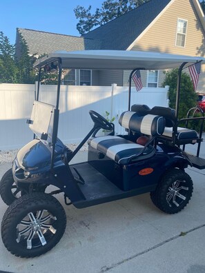 En golfbil parkerad framför ett hus med ett vitt staket och en amerikansk flagga.