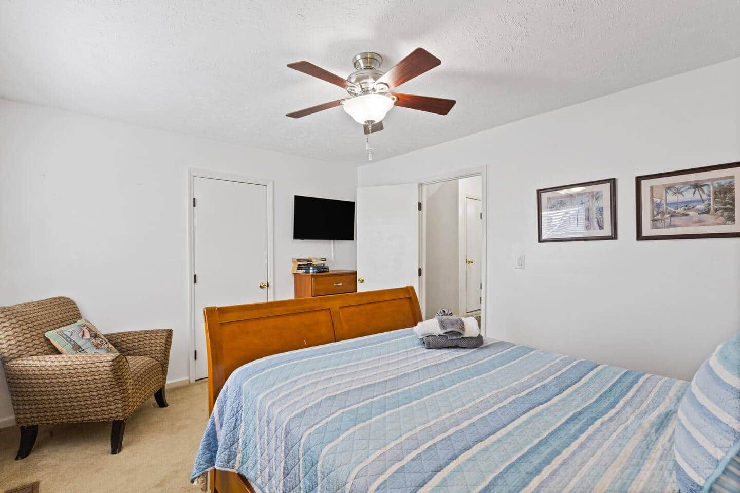 Ein Schlafzimmer mit einem Bett, einem Sessel, einem Deckenventilator, einem Fernseher und gerahmten Bildern an der Wand.