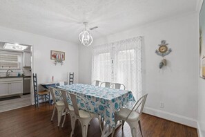 Zona pranzo con tavolo apparecchiato per quattro, cucina sullo sfondo e un orologio decorativo a parete.
