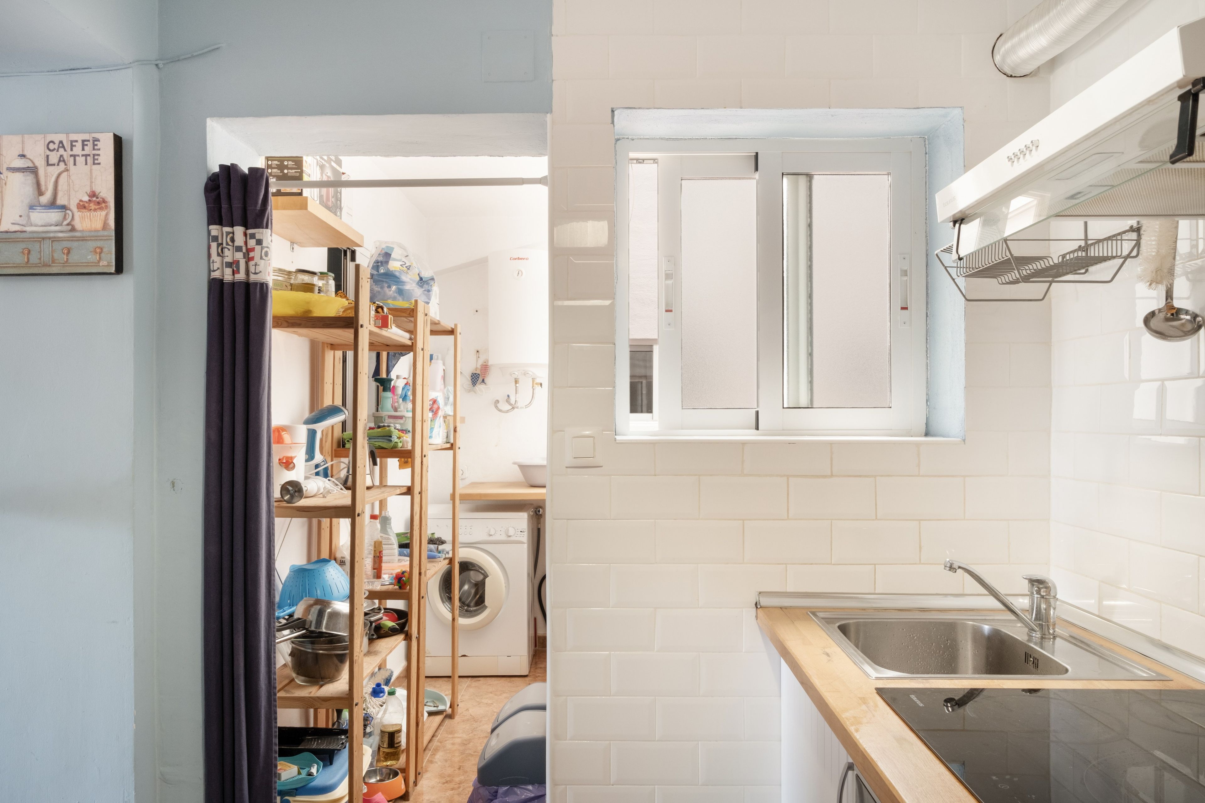 Une cuisine compacte équipée d’un lave-linge intégré, d’une petite fenêtre et d’une étagère où sont rangés divers objets.