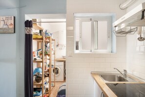 Cozinha compacta com máquina de lavar embutida, uma janela pequena e uma prateleira com diversos objetos.