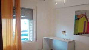 Ein Schlafzimmer mit zwei Betten, einem Deckenventilator, einem Fenster mit Vorhängen und einem an der Wand befestigten Regal.