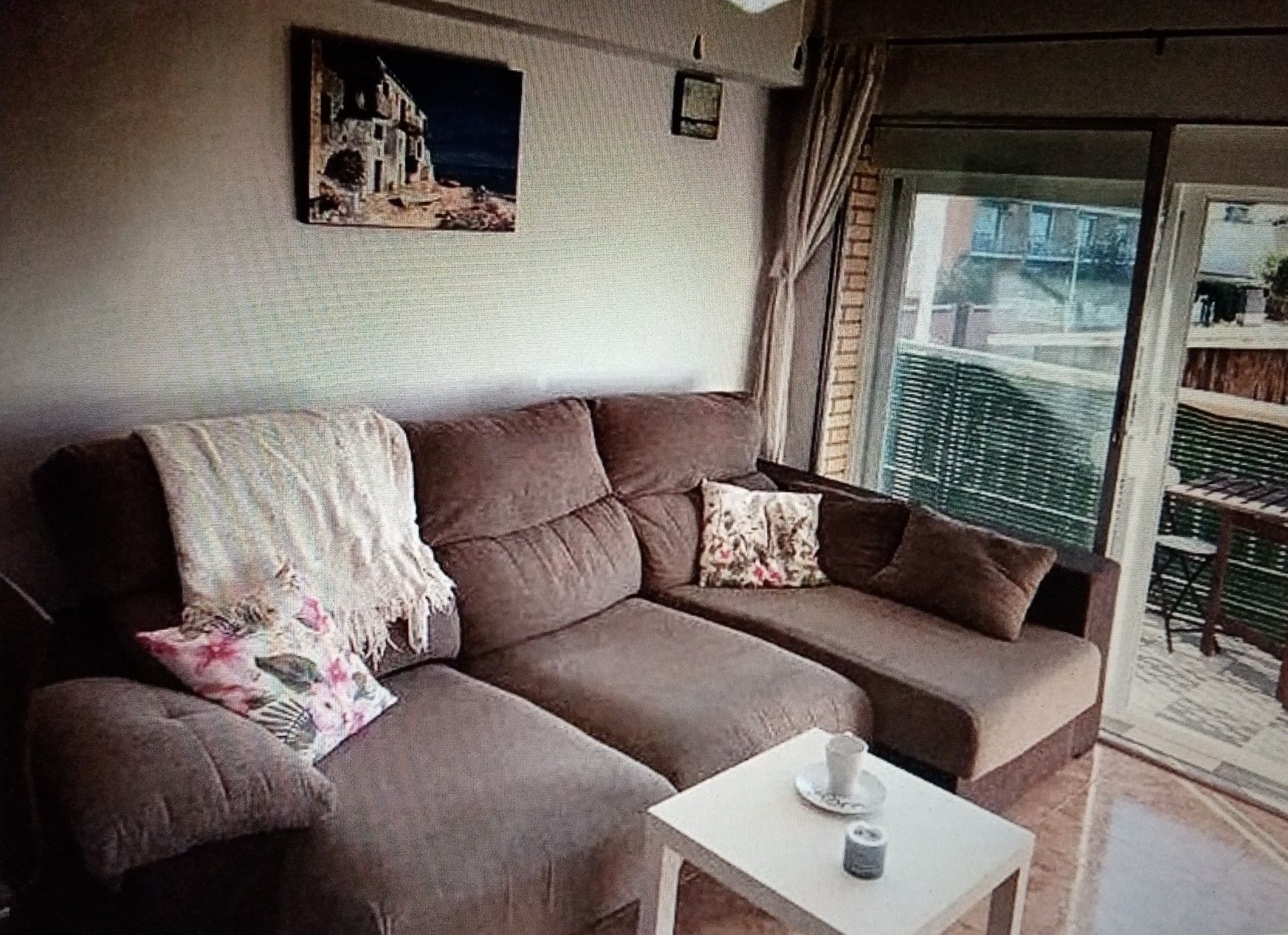 Un divano marrone con un tavolo bianco e una tazza, un quadro al muro e vista sull'esterno.