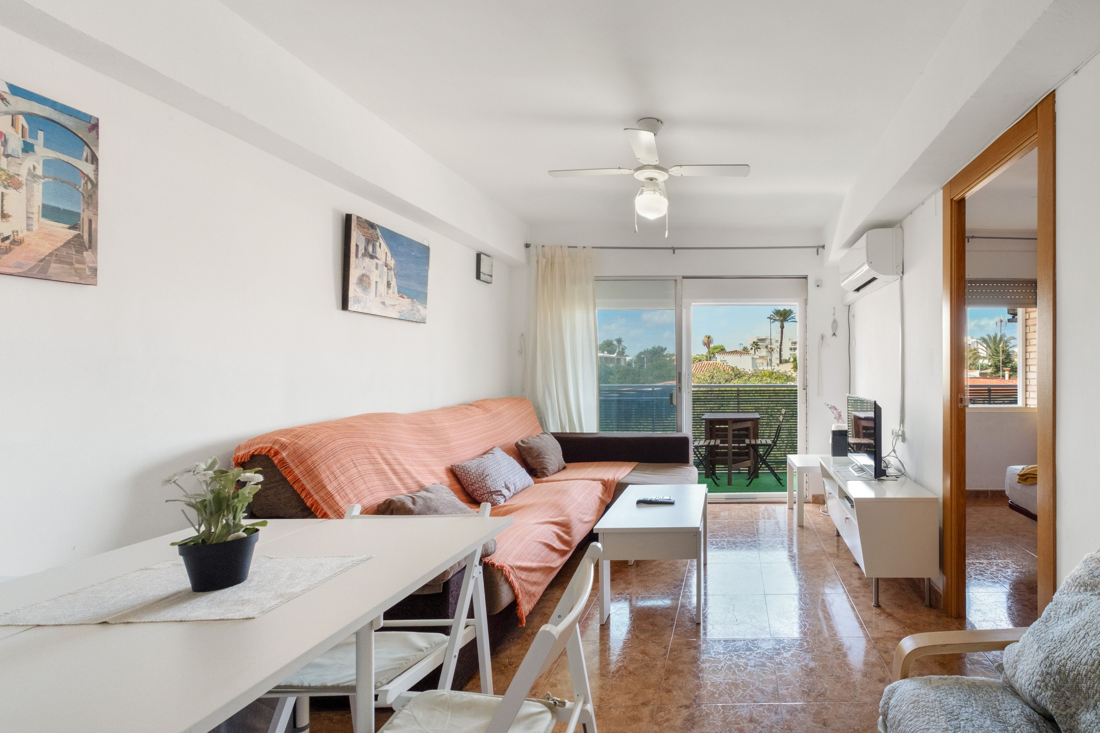 Una sala moderna con sofá, mesa de comedor y televisión. Cuenta con un balcón con vistas a la ciudad.