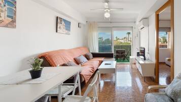 Una sala moderna con sofá, mesa de comedor y televisión. Cuenta con un balcón con vistas a la ciudad.