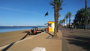 Eine Strandansicht mit einer Rettungswache, einem geparkten Fahrzeug und freiem Blick auf das Meer.