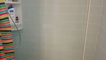 Zona de ducha con pared de azulejos, cabezal de ducha y un estante con artículos de aseo.