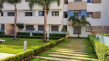 A modern multi-story residential building with a central courtyard featuring a patterned walkway, palm trees, and well-maintained greenery.