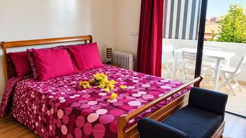 A bedroom with a bed, a bedside table, a lamp, a window with curtains, and a view of the outside.