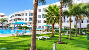 A hotel pool area with sun loungers, palm trees, and a clear blue sky.