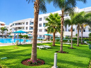 A hotel pool area with sun loungers, palm trees, and a clear blue sky. - Beautiful 2-bedroom Apartment With Pool View Mohammedia (El Mansouria)