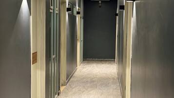 A hallway with doors on both sides, a trash bin in the foreground, and a tiled floor.